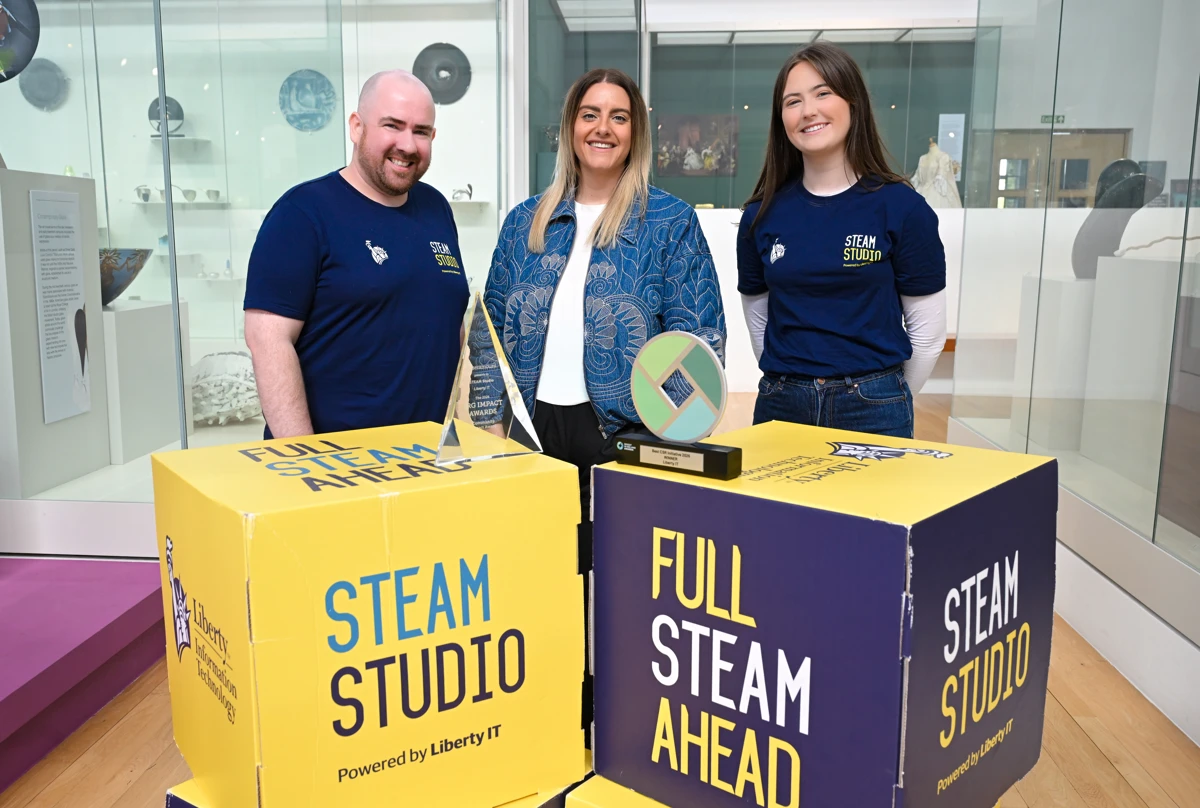 Three Liberty IT employees standing in museum setting with awards and STEAM Studio branding