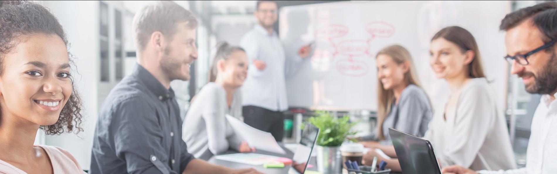 Photo of a people at a table with a man writing on a whiteboard in the background