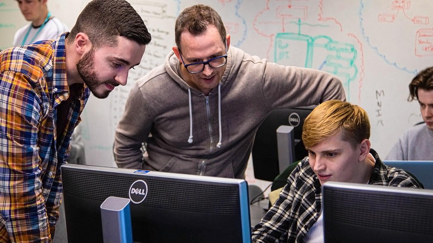 Photo of three men looking at a screen - two standing; one seated