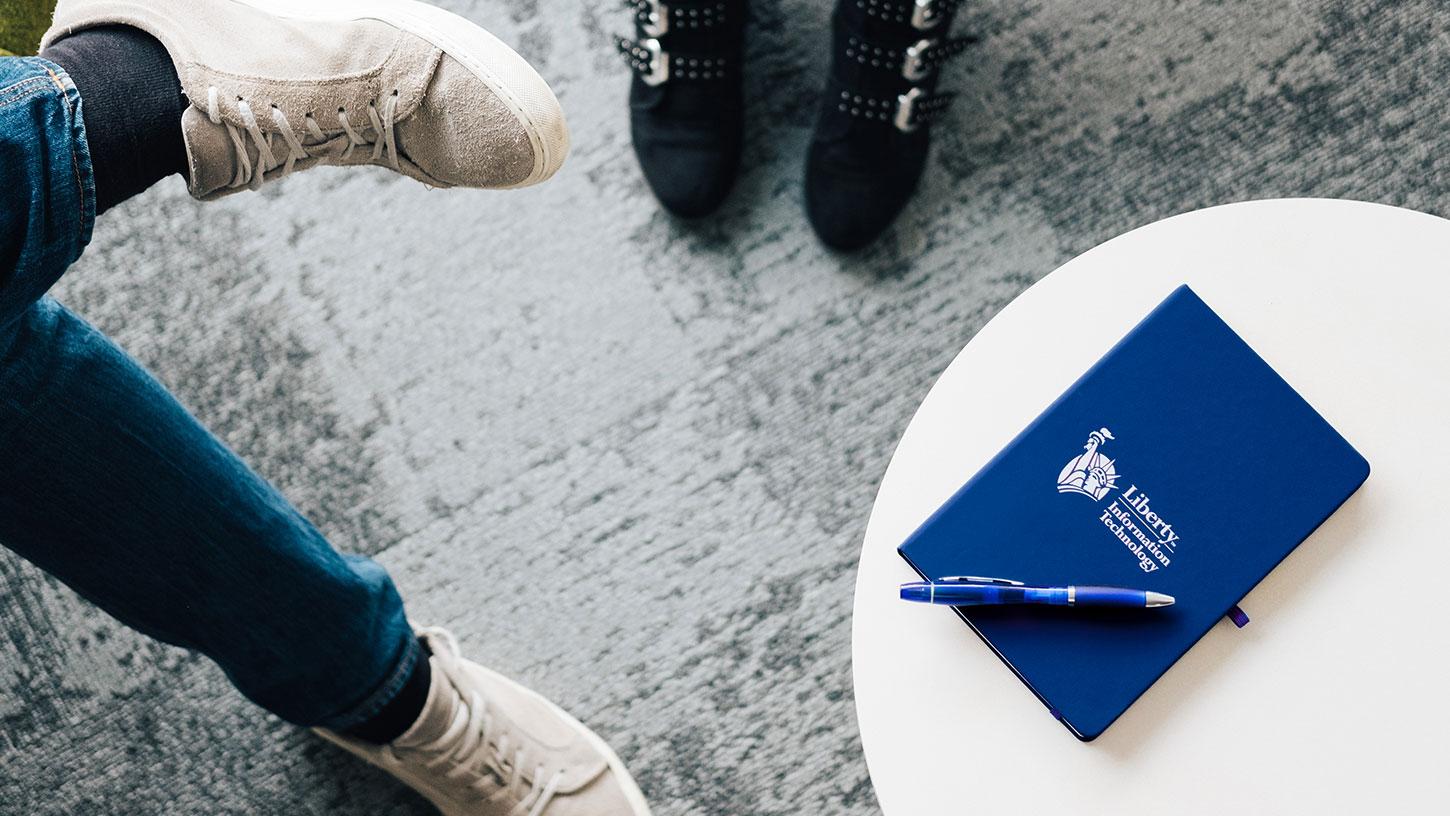 Photo of a Liberty It notebook on a white table beside two pairs of feet