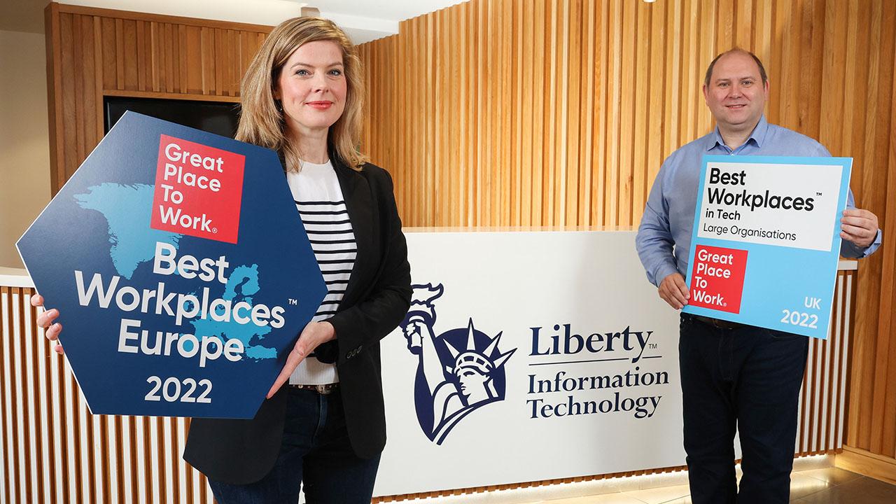 Two people standing in front of a Liberty IT logo, holding Great Place to Work Logos