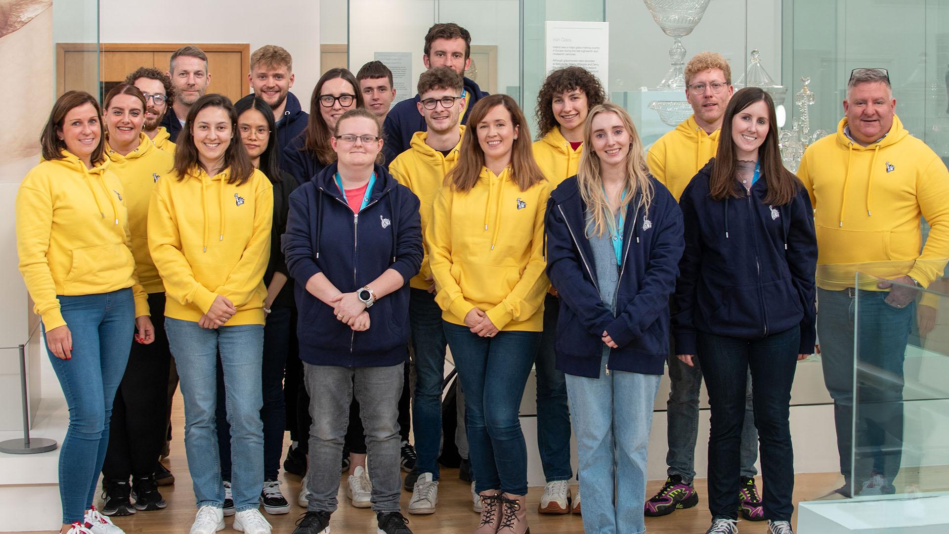 (slide 1 of 9) Group of Liberty IT employees, who are STEAM Studio Ambassadors, in branded hoodies standing in the Ulster Muesum. 